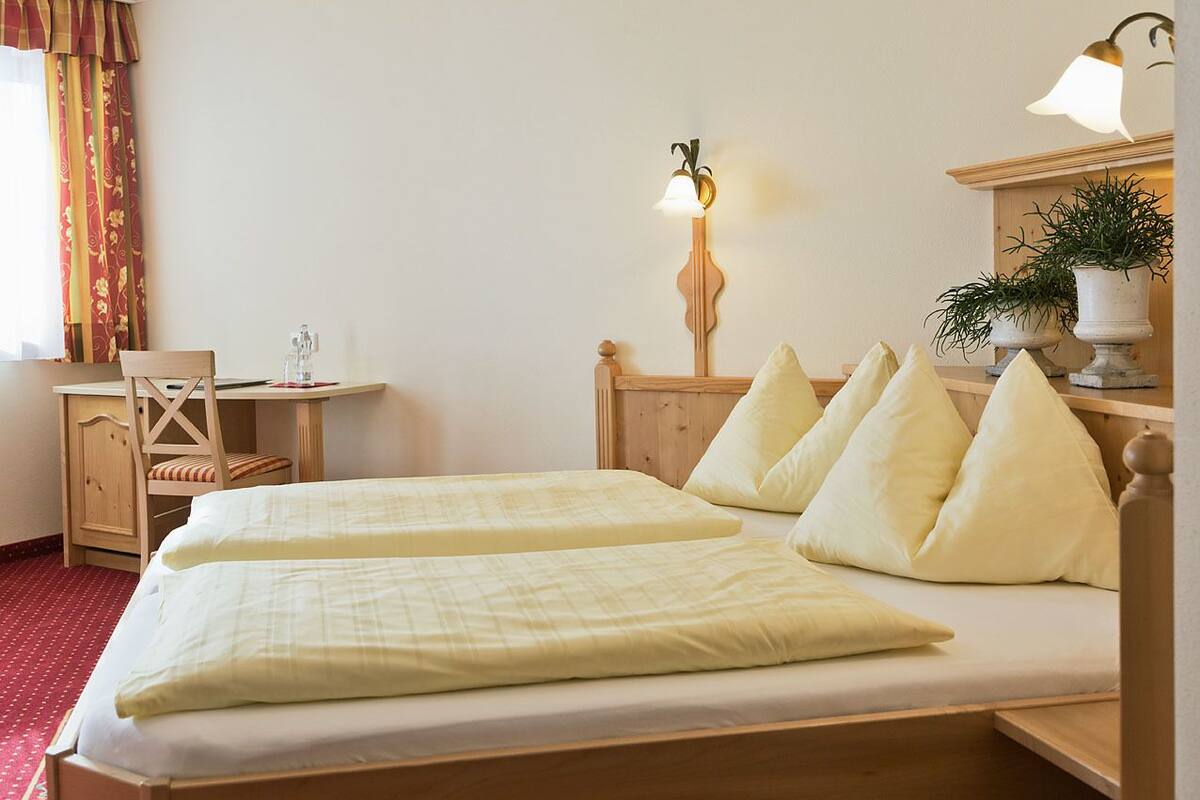 Ein Hotelzimmer mit zwei Betten, einem Schreibtisch, einem Stuhl, einer Lampe und einem Blumentopf.