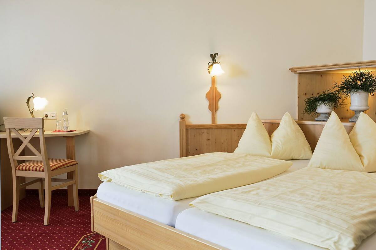 Ein Hotelzimmer mit zwei Betten, einem Schreibtisch, einem Stuhl, einer Lampe und einem Spiegel, dekoriert mit Pflanzen.