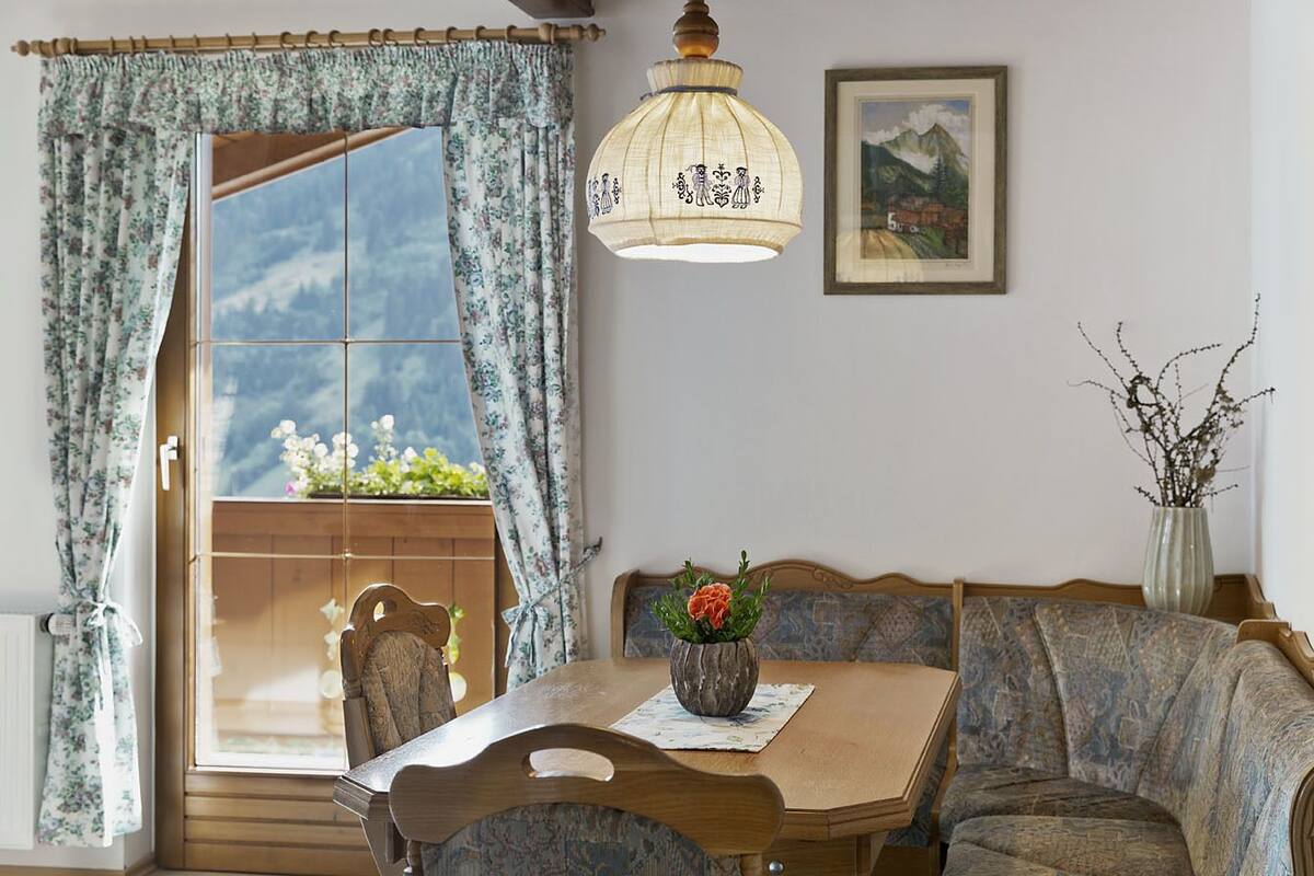 Ein Essbereich mit einem Holztisch, Stühlen, einer Vase mit Blumen, einer Hängelampe und einem Fenster mit Vorhängen.