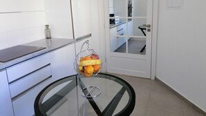 A modern kitchen with white cabinets, a glass countertop, and a round glass table with a fruit basket. - Luxurious Apartment in le Palace (La Marsa)
