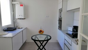 A compact kitchen with white cabinets, a built-in oven, a coffee maker, and a glass table with a decorative item. - Luxurious Apartment in le Palace (La Marsa)