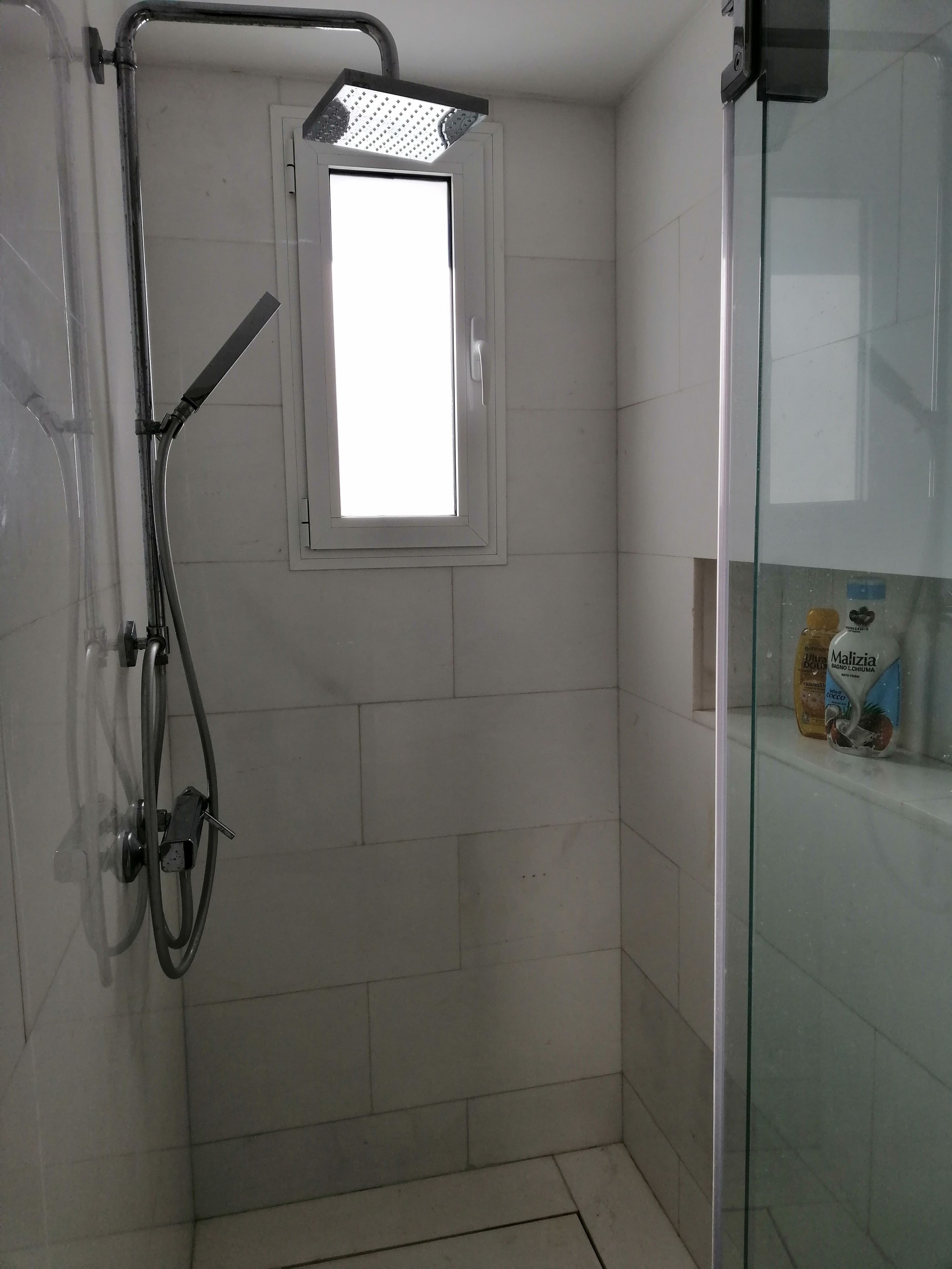 Une douche avec une fenêtre, des murs carrelés et une porte de douche en verre.