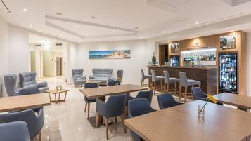 A modern hotel lobby with seating areas, a bar, and a large painting on the wall.