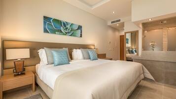 Une chambre d’hôtel moderne dotée d’un grand lit, d’une table de chevet avec une lampe, d’une œuvre d’art accrochée au mur, et d’une salle de bain avec un meuble-lavabo et un miroir.