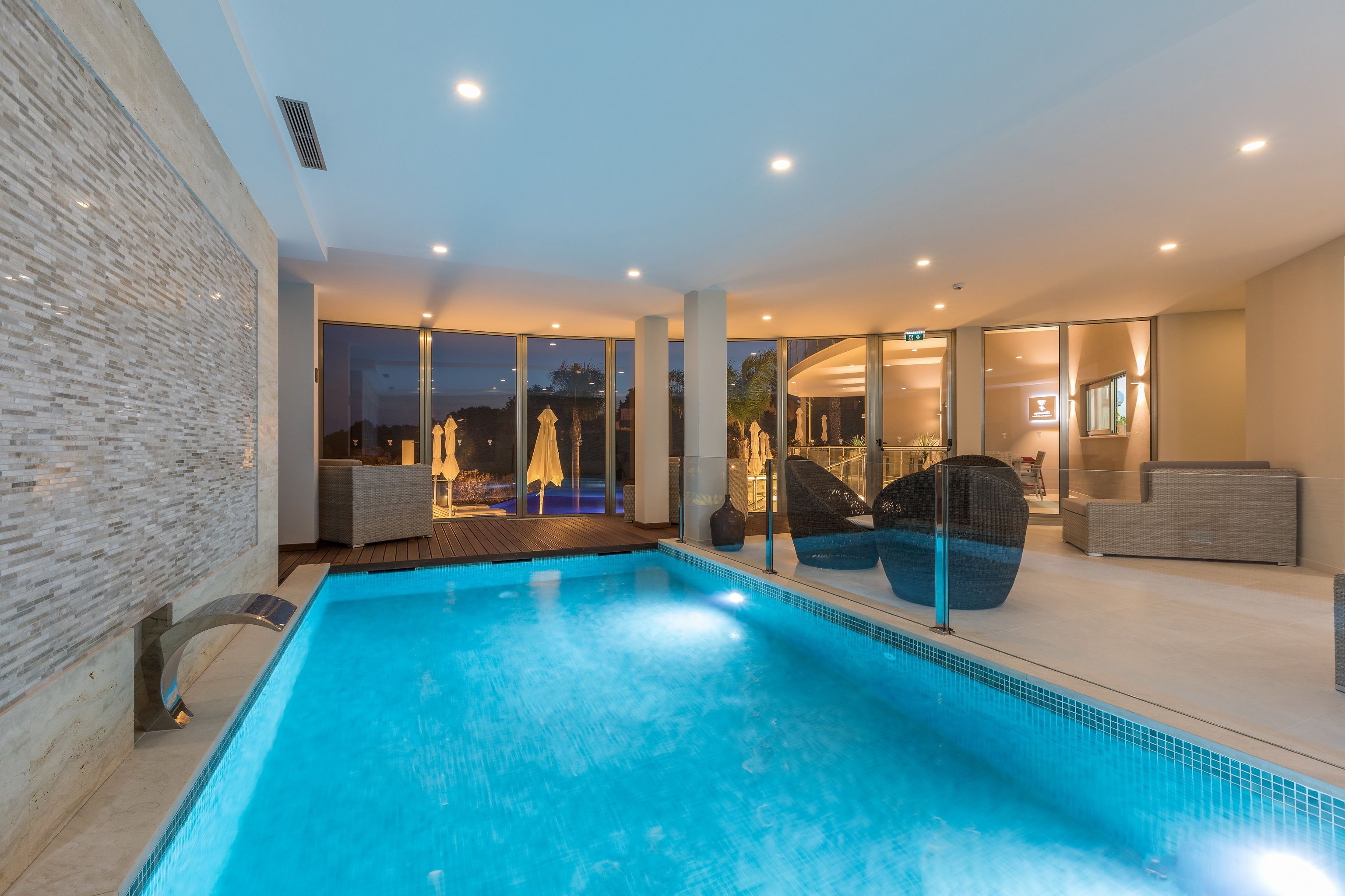 Una piscina interior moderna con paredes de vidrio transparente, asientos cómodos y vistas al exterior.