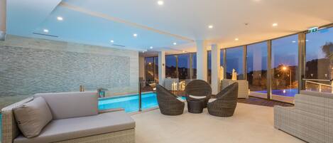 Un área de descanso al aire libre con piscina, muebles de mimbre y amplias ventanas que ofrecen vistas de la piscina y el cielo.