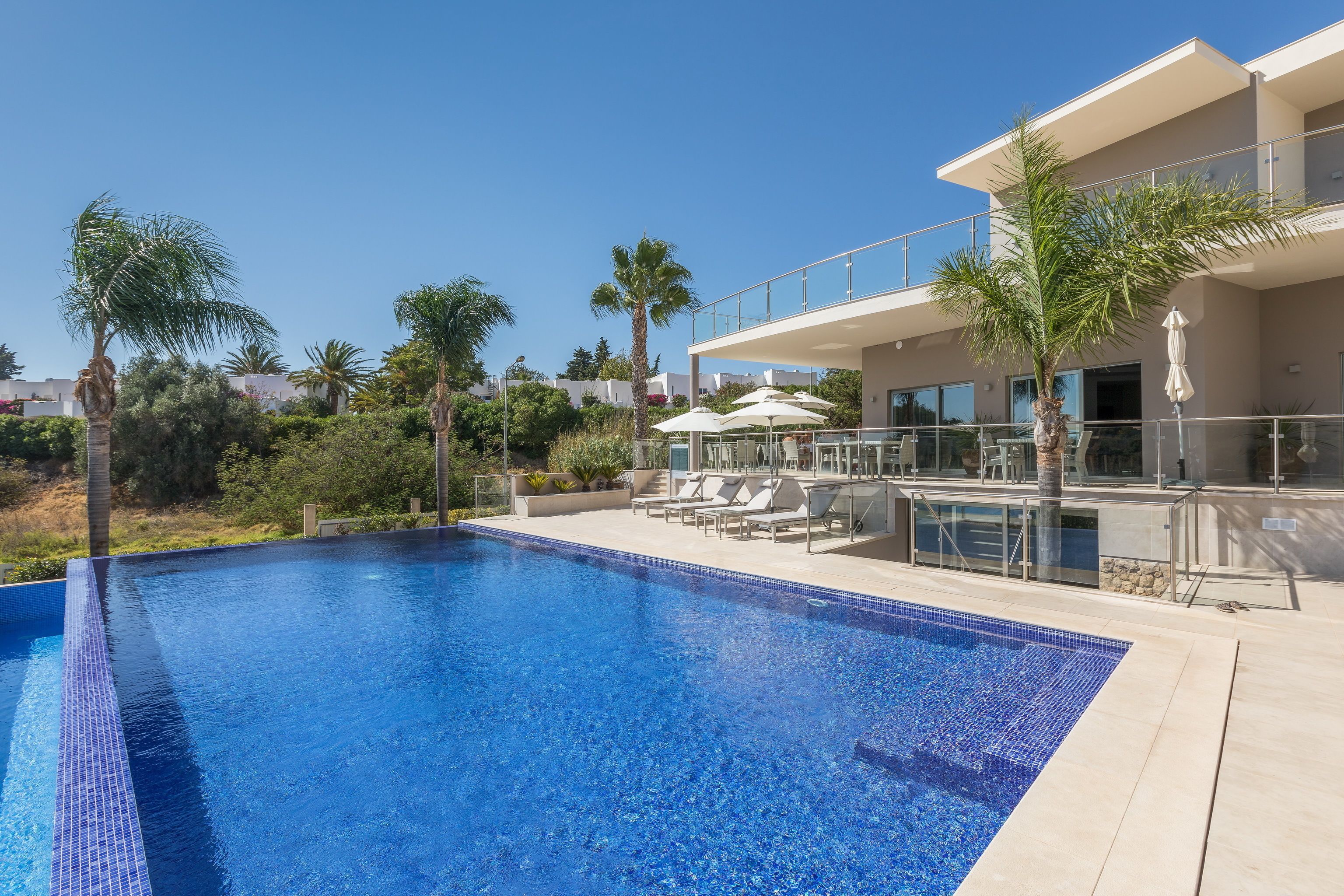 A modern hotel with a swimming pool, sun loungers, and palm trees.