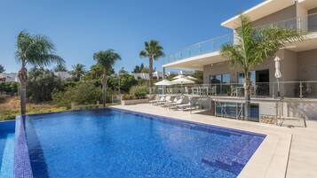 A modern hotel with a swimming pool, sun loungers, and palm trees.