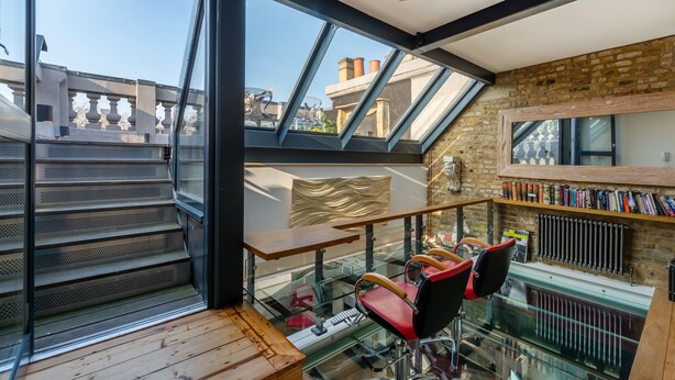 A modern interior with a glass staircase, a wooden table, and a red chair. - The Museum Penthouse (London)