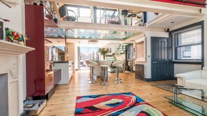 A spacious living area with a high ceiling, a glass staircase, and a modern kitchen in the background. - The Museum Penthouse (London)
