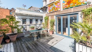 A wooden deck with a table and chairs, potted plants, and a building with a colorful mural. - The Museum Penthouse (London)