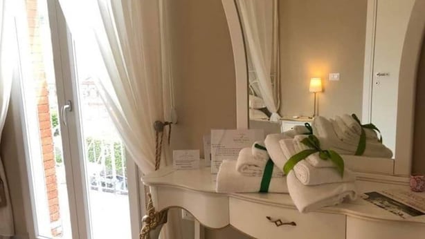 A hotel room with a vanity, a mirror, a towel rack with neatly folded towels, and a window with curtains. - B&B Baronia Luxury Rooms (Castel Baronia)