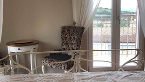A bedroom with a bed, a chair, a small table, and a balcony with a railing. - B&B Baronia Luxury Rooms (Castel Baronia)