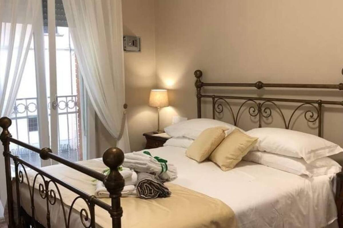 Un lit bien fait, avec du linge de lit blanc et des oreillers beige, une lampe de chevet et un cadre de lit en métal.
