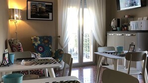 A room with a dining table, chairs, a lamp, a painting, a television, and a kitchen area with cabinets and appliances. - B&B Baronia Luxury Rooms (Castel Baronia)