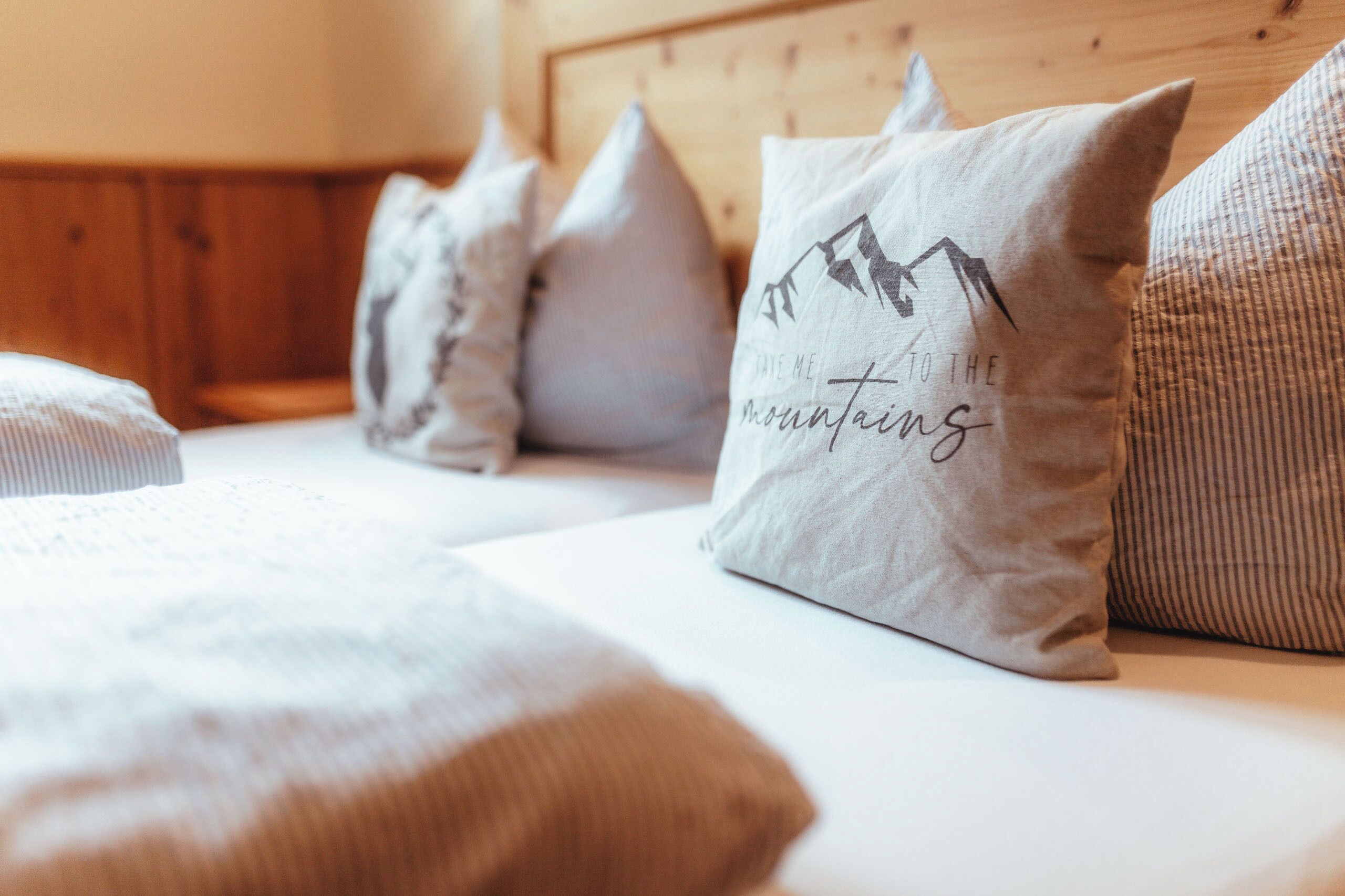 A bed with multiple pillows, one with a mountain design and text.