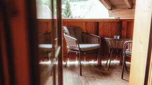 Eine Holzterrasse mit Korbstühlen und einem Tisch, eine Holzbeschichtung und Blick auf Grünlandschaft.