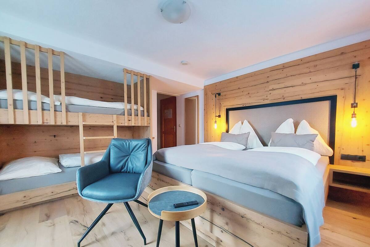 Une chambre avec un lit superposé, un lit simple, une chaise bleue et une petite table en bois.
