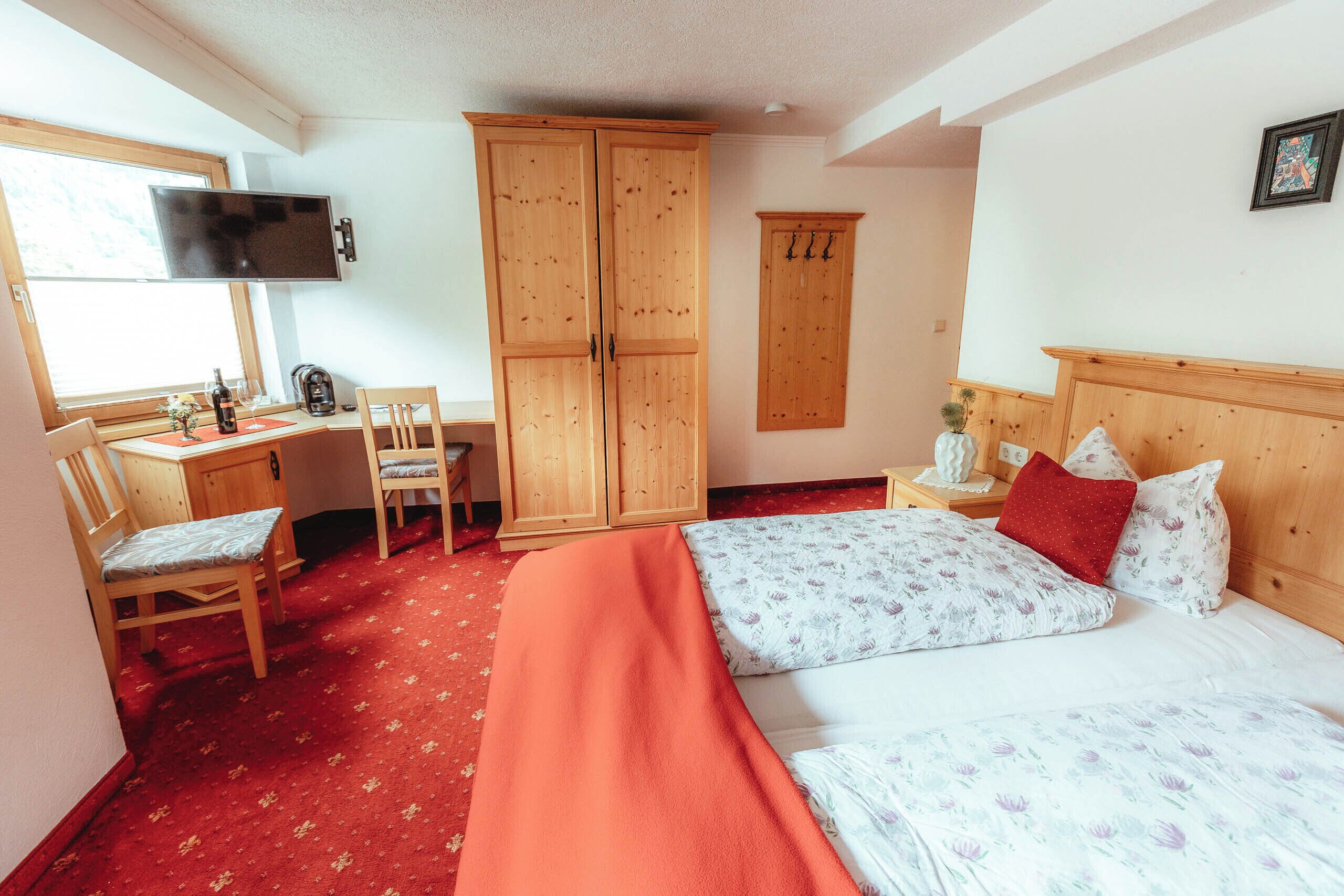 A bedroom with a bed, a desk, a chair, a wardrobe, and a television.