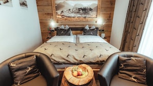 Ein Schlafzimmer mit einem Bett, zwei Nachttischen, einem Holz-Kopfende, einem Wandbild, einem Fenster mit Vorhängen und einem kleinen Holztisch mit Obst.