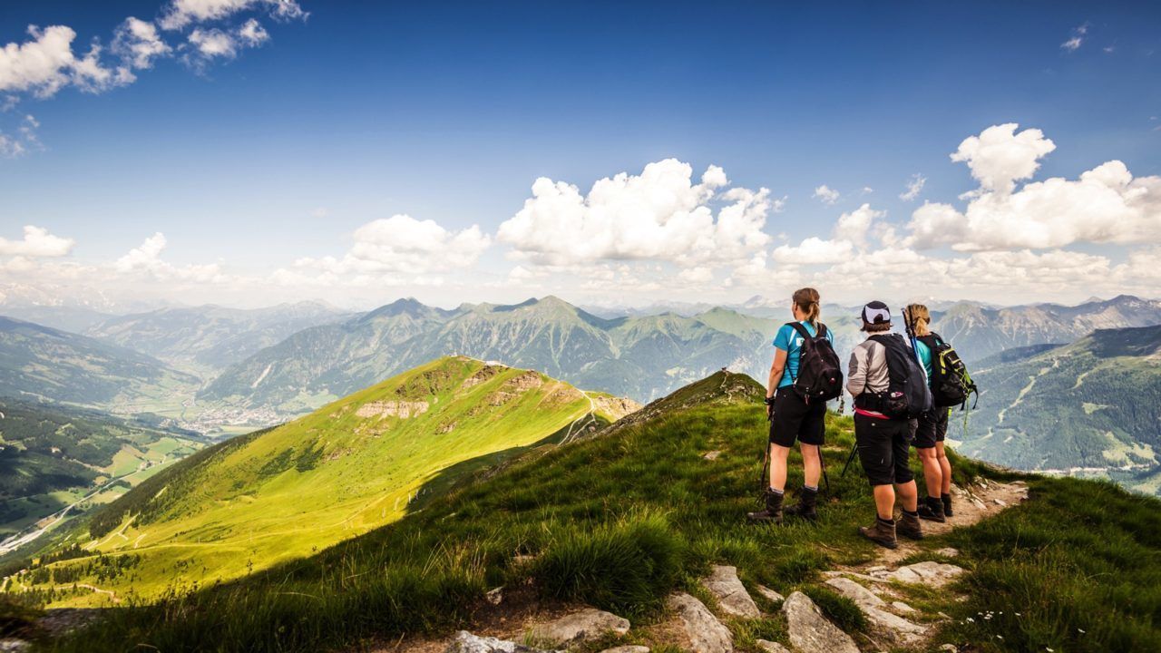 Eine Gruppe Wanderer auf einem Bergpfad mit einem weiten Panoramablick auf die umliegende Landschaft.