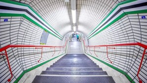 Una estación de metro con techo curvo, barandales de seguridad rojos y una escalera hacia una salida.