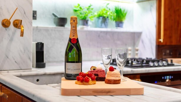 Una cocina con encimera de mármol, una botella de champán Moët & Chandon, dos copas y una tabla de madera con postres.