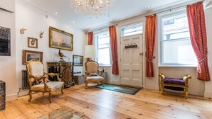 Quarto espaçoso com assoalho de madeira, um candelabro e uma grande janela com cortinas vermelhas.
