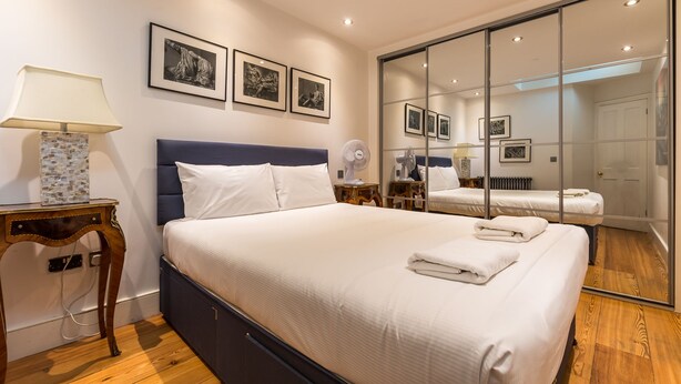 Um quarto moderno com uma cama grande, mesas de cabeceira, um espelho e quadros nas paredes.