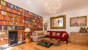 Uma sala de estar ampla com lareira, um sofá vermelho, uma mesa de centro e uma grande estante repleta de livros.