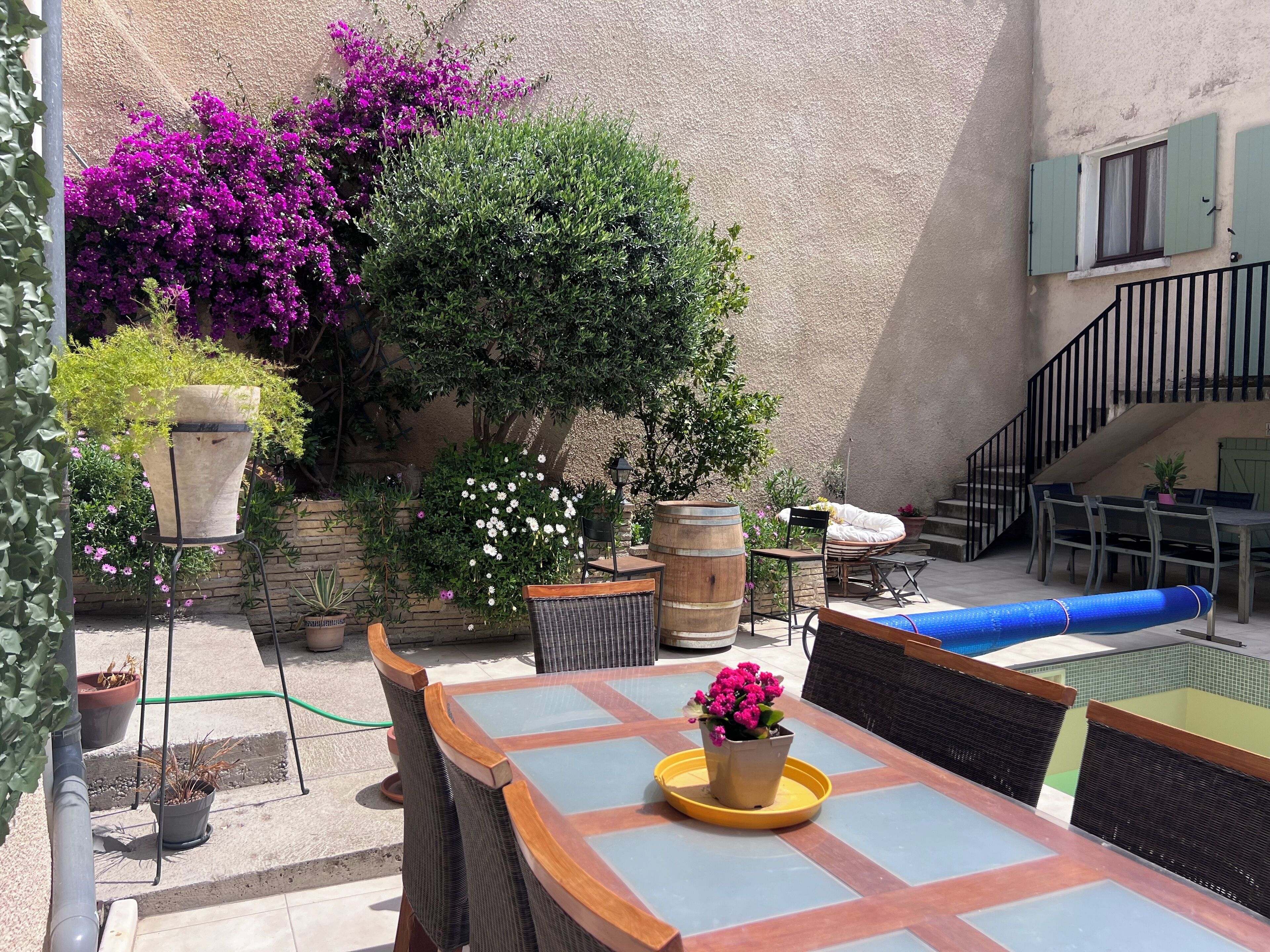 An outdoor patio with a table and chairs, surrounded by potted plants and a staircase.