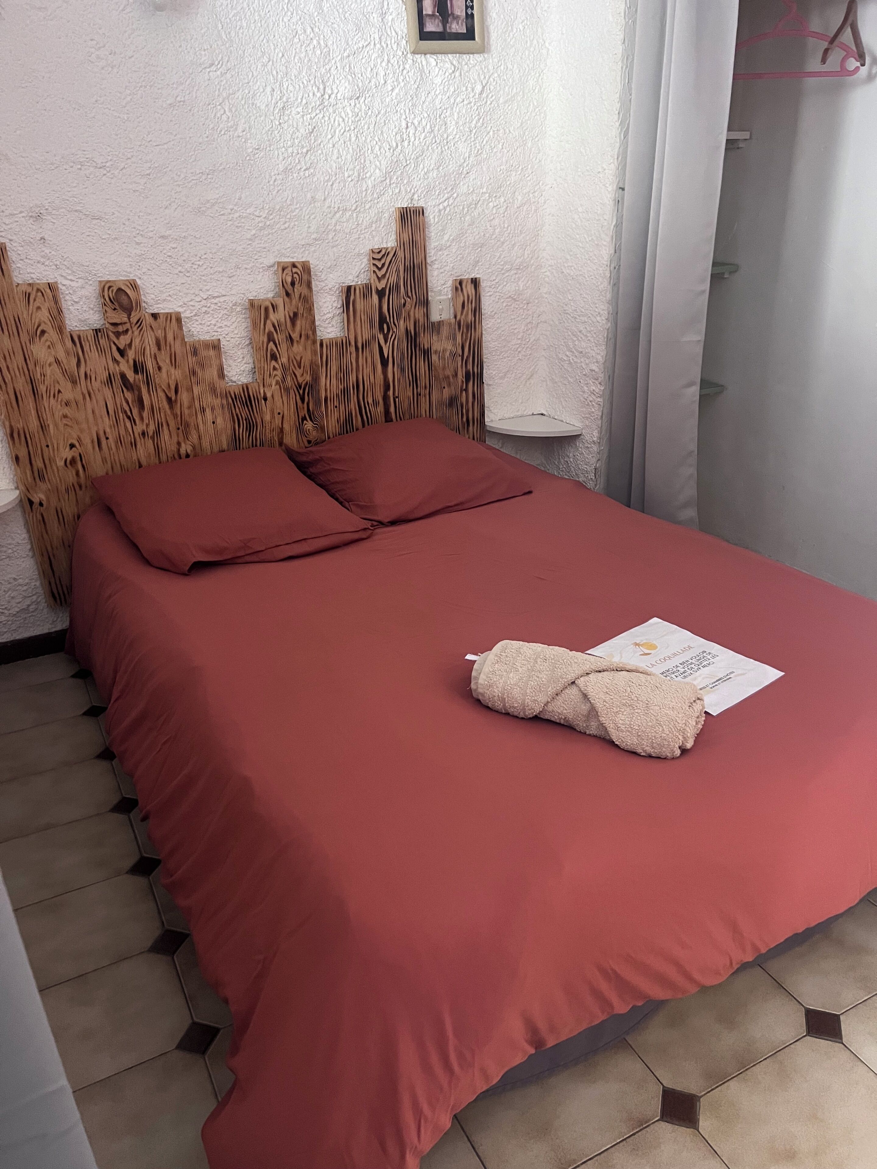 Een bed met een rode sprei, twee rode kussens en een beige handdoek op het bed.