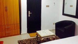 Una habitación con un armario de madera, una puerta negra, una mesita con un libro, un sillón negro y un aire acondicionado instalado en la pared.