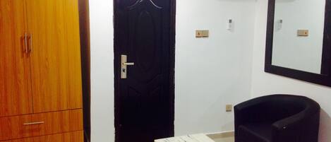 Una habitación con un armario de madera, una puerta negra, una mesita con un libro, un sillón negro y un aire acondicionado instalado en la pared.