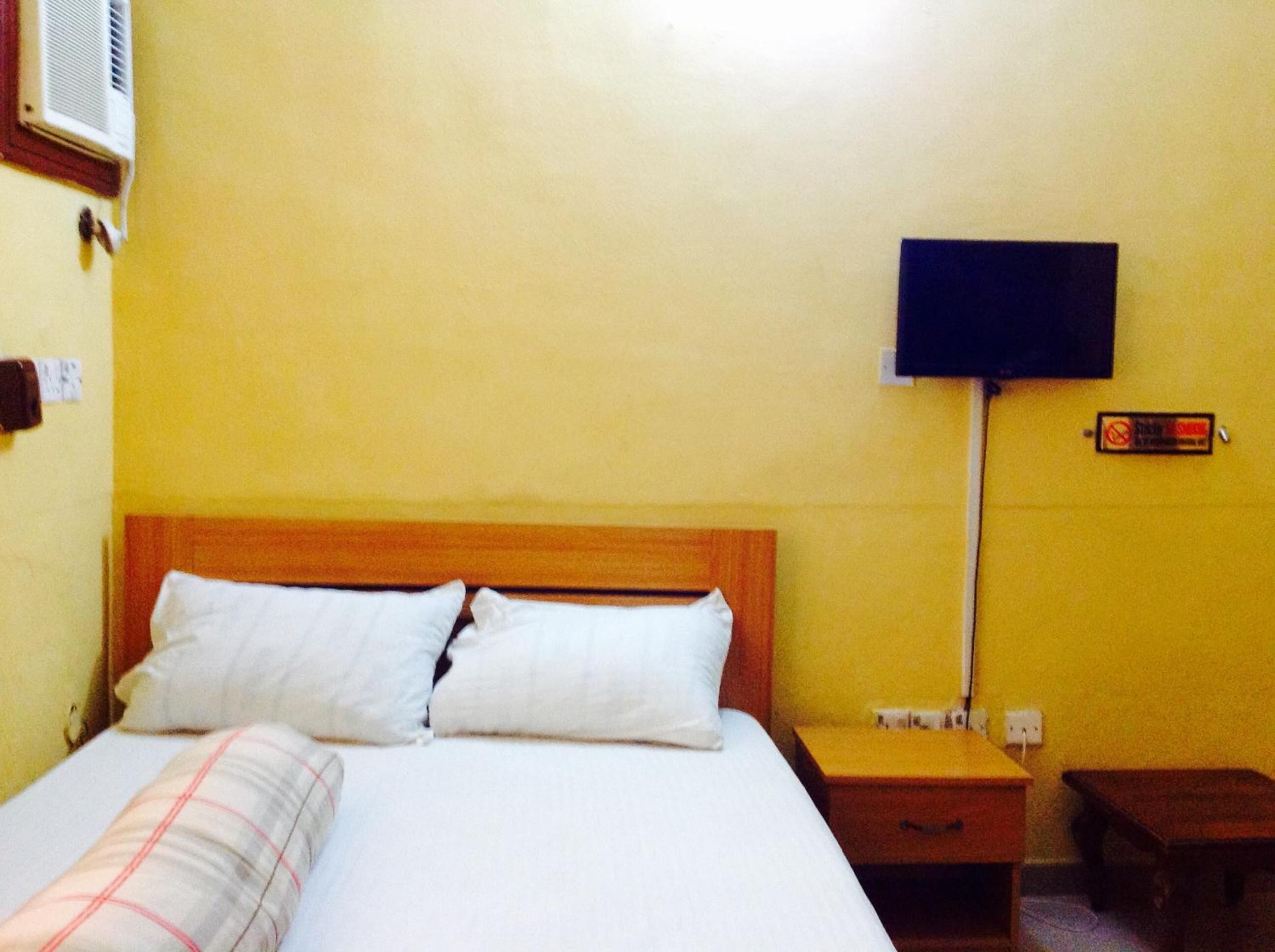 Habitación de hotel con una cama, una mesita de noche, un televisor montado en la pared y un cartel de prohibición de fumar.