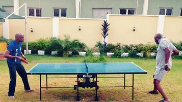 Enjoy a game of ping pong in the serene outdoor setting, surrounded by lush landscaping and a charming building in the background.