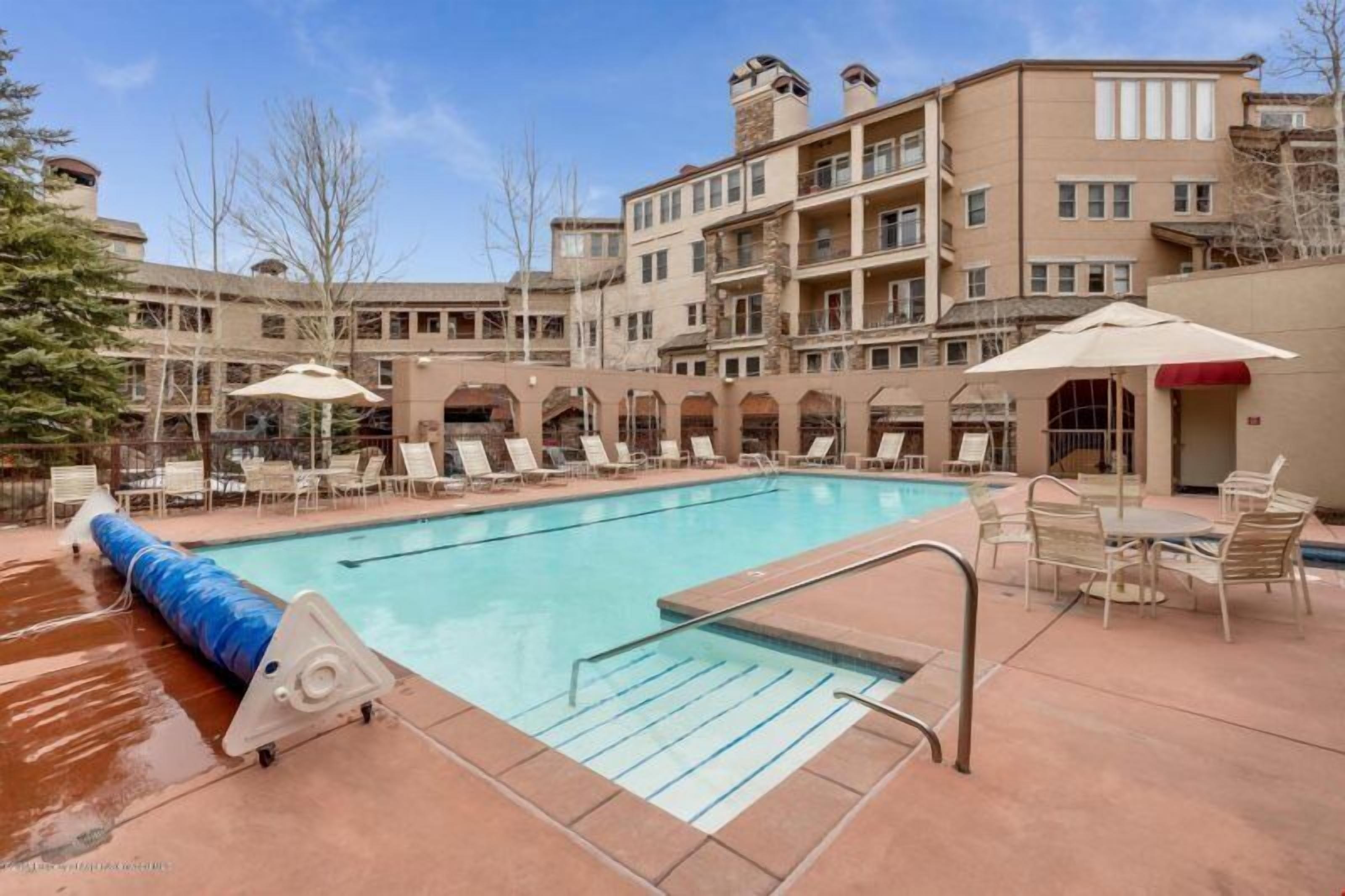 A swimming pool with lounge chairs and umbrellas, surrounded by multi-story buildings with balconies.