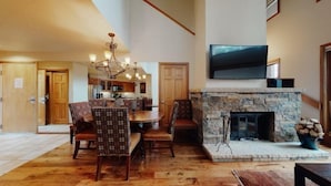 A spacious living room with a stone fireplace, wooden flooring, and a dining area with patterned chairs.