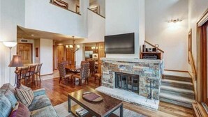A spacious living area with a stone fireplace, a flat-screen TV mounted above it, and a dining area with wooden furniture.