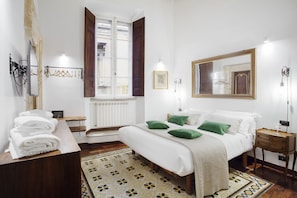 Een slaapkamer met een bed, een dressoir, een spiegel en een raam met luiken.
