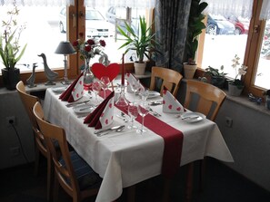 A dining table set for two with white tablecloths, red napkins, and heart-shaped place settings. - Haus Waldesruh (Hollnich)