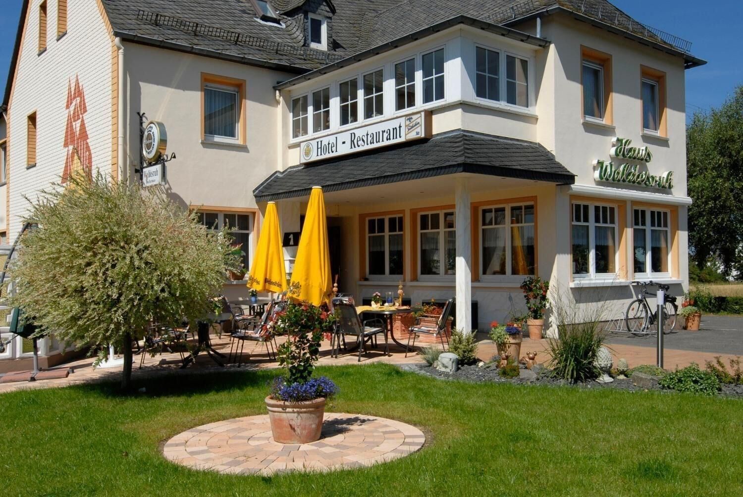 Ein Hotel mit Restaurant im Erdgeschoss, Außenbereich mit gelben Sonnenschirmen und einem gepflegten Garten.