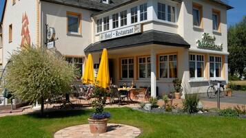 Ein Hotel mit Restaurant im Erdgeschoss, Außenbereich mit gelben Sonnenschirmen und einem gepflegten Garten.
