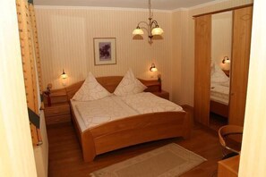 A bedroom with a wooden bed, two bedside lamps, a framed picture on the wall, and a mirror on the door. - Haus Waldesruh (Hollnich)