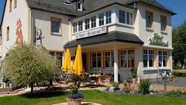Ein Hotel mit Restaurant im Erdgeschoss, Außenbereich mit gelben Sonnenschirmen und einem gepflegten Garten.