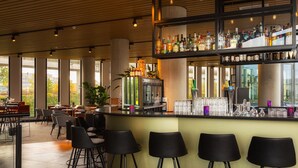 A modern bar area with a high bar counter, multiple seating options, and a variety of bottles and glasses. - Postillion Hotel Amsterdam (Amsterdam)