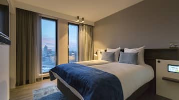 A modern hotel room with a large bed, a control panel, and a view of the cityscape through the window.