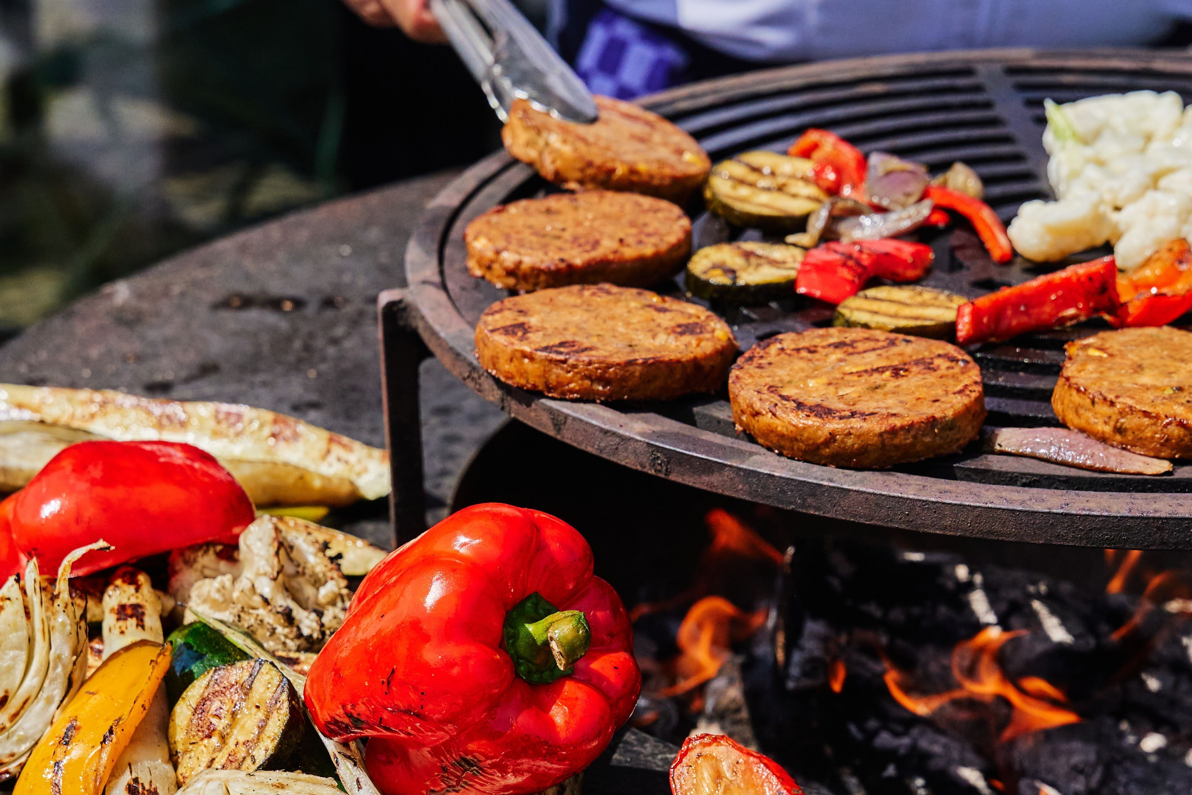 Una parrilla con hamburguesas, verduras y un pimiento rojo.