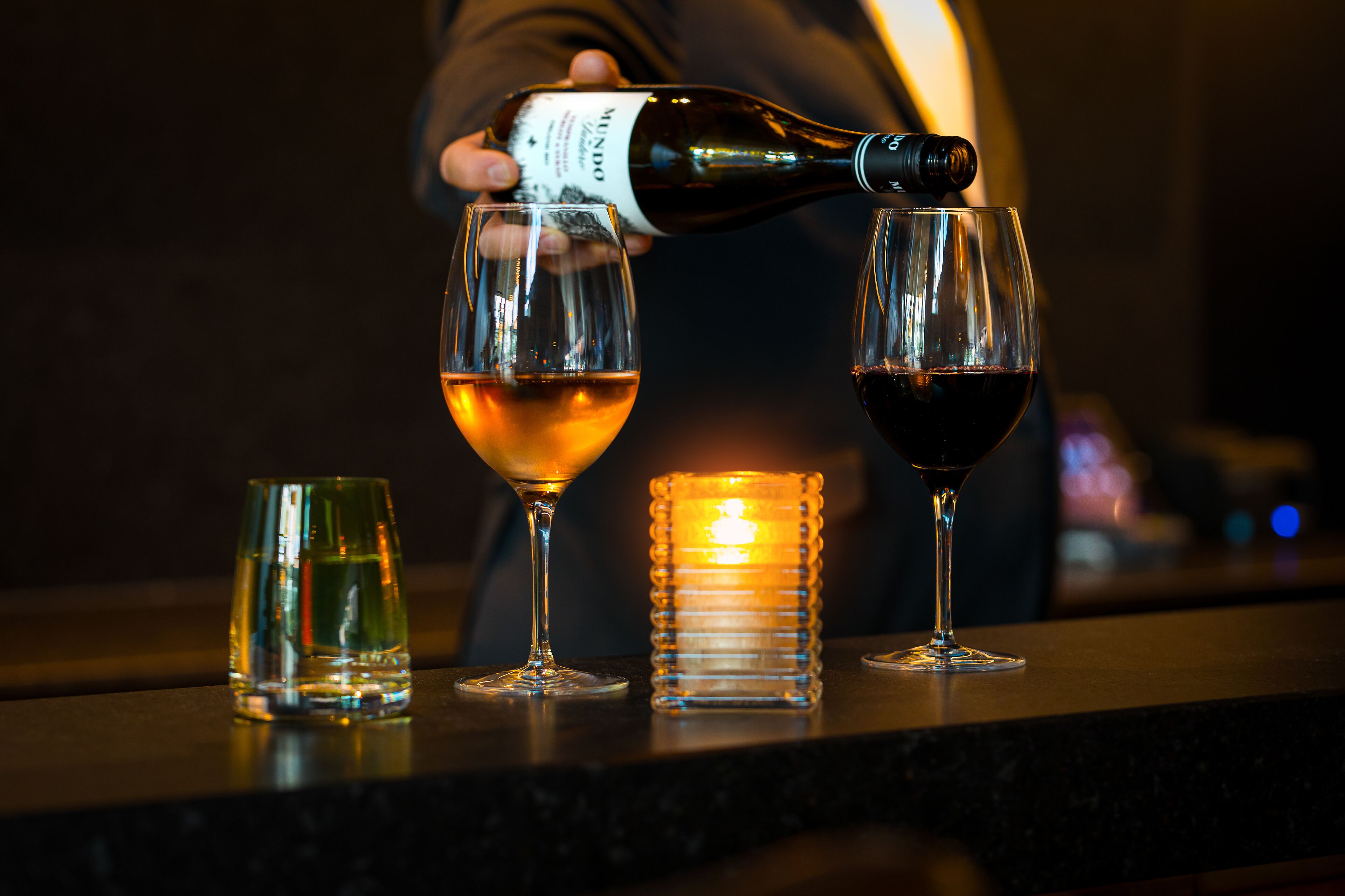 Una persona sirve vino en dos copas sobre una barra.