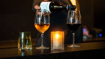 A person pouring wine into two glasses on a bar counter.